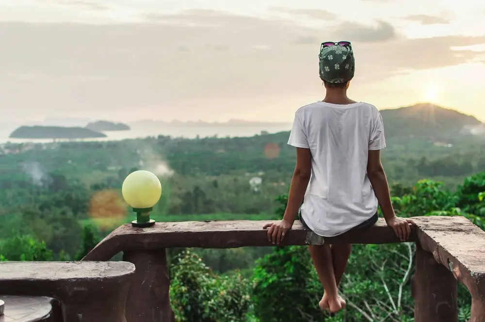 Image of woman sitting on a bench infront of beach view, solo travel