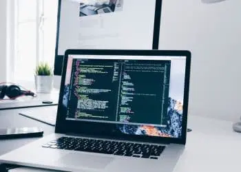 A MacBook with lines of code on its screen on a busy desk